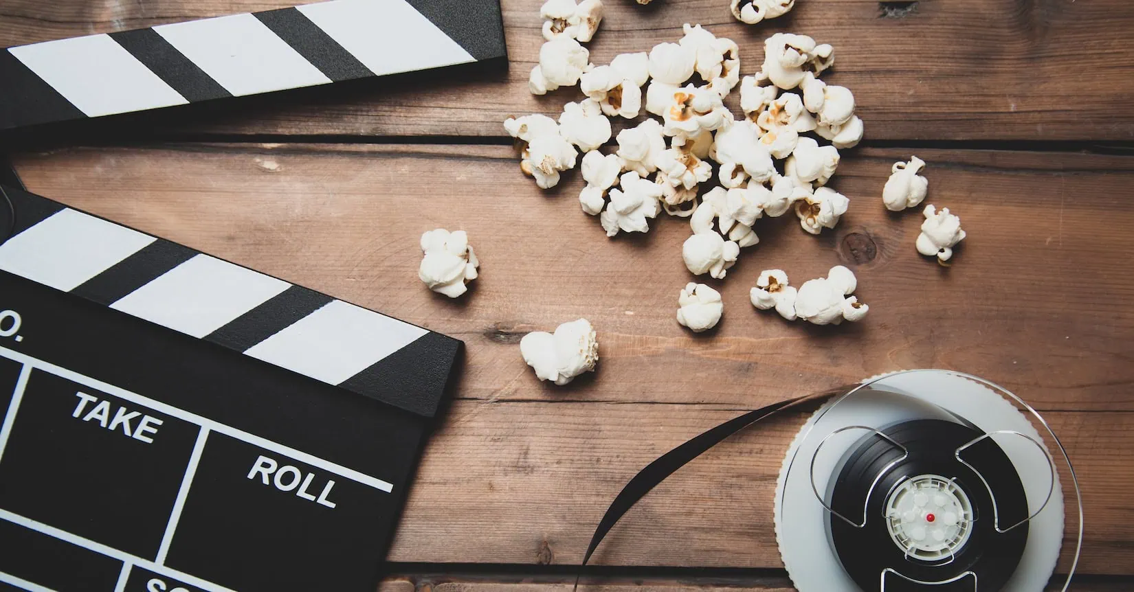 Closeup of movie camera with film reel clapper board and popcorn on wood